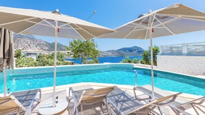 A pool area with lounge chairs and umbrellas, a clear blue sky, and a mountainous backdrop. - Kalkan Saray Suites - Adults Only (Kas)