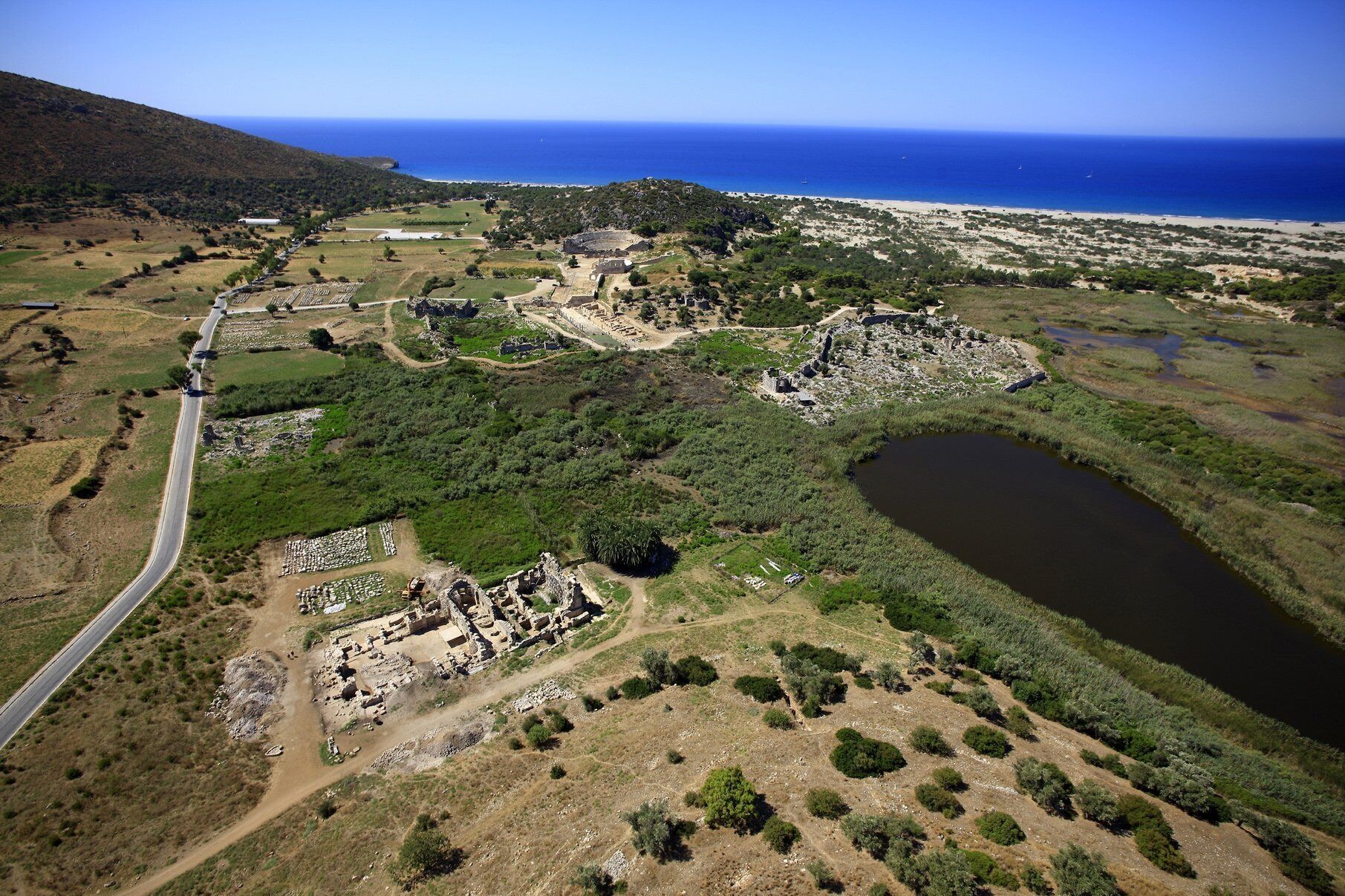 Vista aérea de un sitio arqueológico con ruinas, una carretera y una masa de agua.