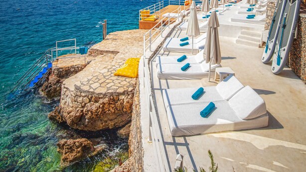 A seaside hotel with a stone terrace, sun loungers, and umbrellas. - Kalkan Saray Suites - Adults Only (Kas)