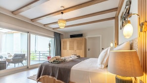 A bedroom with a large bed, a wooden ceiling, a balcony with chairs, and a view of greenery. - Kalkan Saray Suites - Adults Only (Kas)