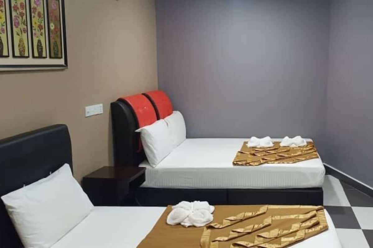 Une chambre d’hôtel avec deux lits, un sol à carreaux et une petite étagère sur laquelle est posé un objet décoratif.