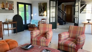 Ein geräumiges Wohnzimmer mit Karoschen Sesseln, einem gemusterten Hocker und einer Holzbalkendecke.