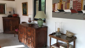 Ein Zimmer mit einem Holzschrank, einem Tisch mit Büchern, einer Lampe und einem Bild an der Wand.