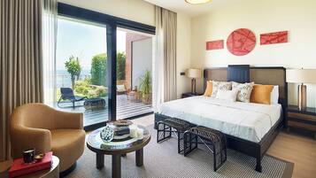 Habitación de hotel con una cama grande, una zona de estar con una silla y una mesa, y vistas al exterior.