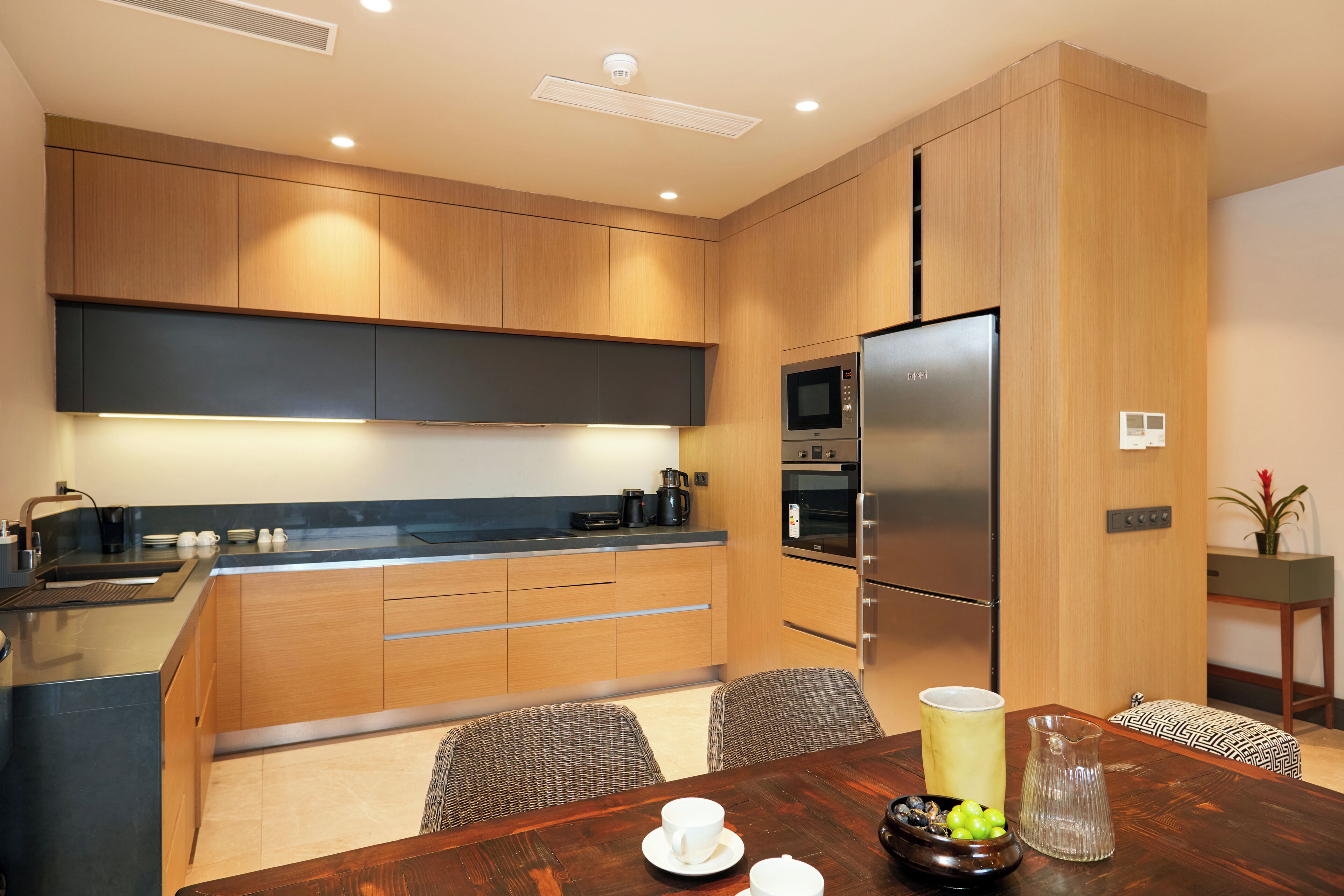 A modern kitchen with wooden cabinets, a stainless steel refrigerator, and a dining area with a wooden table and chairs.