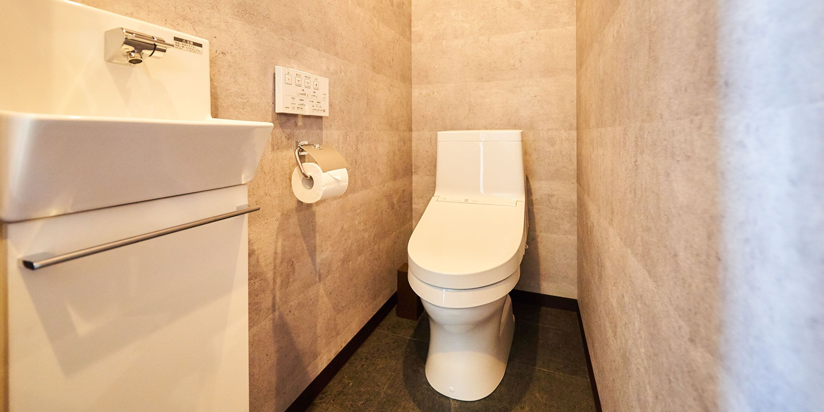 Een compacte, moderne badkamer met toilet, wastafel en een papieren handdoekdispenser.