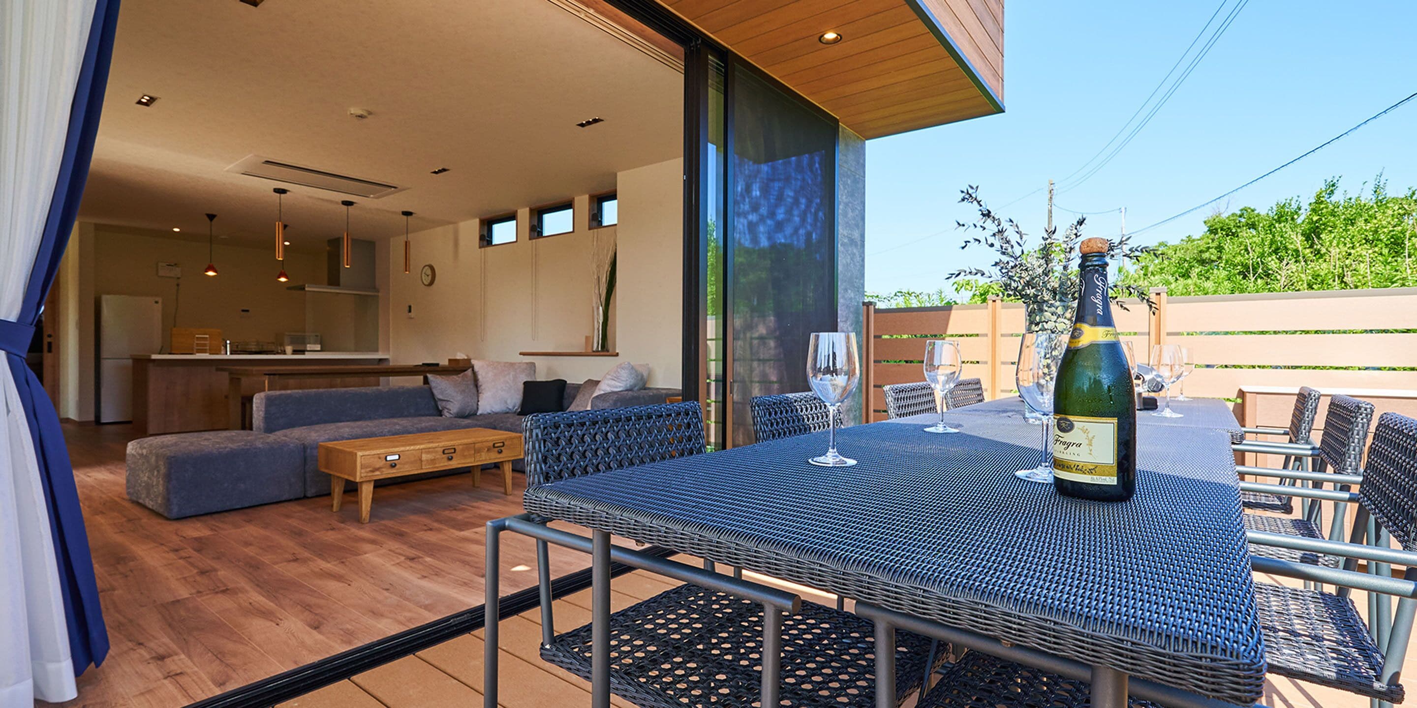 Una cocina moderna con armarios de madera, un comedor con una mesa y sillas azules, y un ventanal con vistas a un jardín.