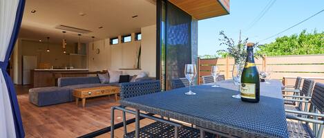Una cocina moderna con armarios de madera, un comedor con una mesa y sillas azules, y un ventanal con vistas a un jardín.