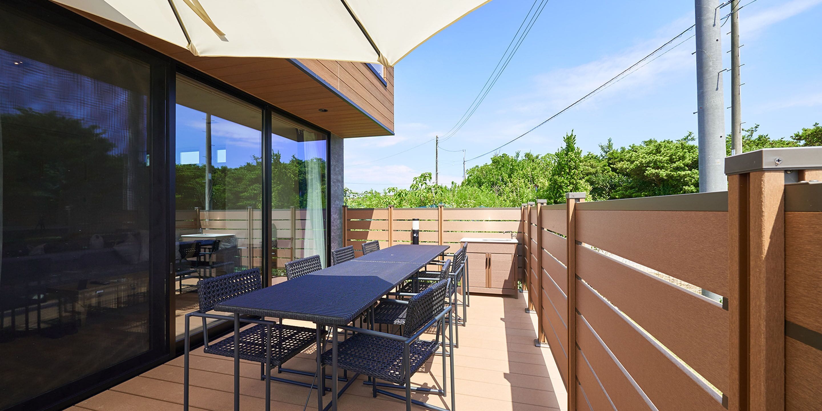 An outdoor patio with a long table and chairs, surrounded by glass walls and a wooden fence.