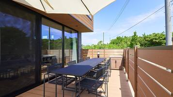 An outdoor patio with a long table and chairs, surrounded by glass walls and a wooden fence.