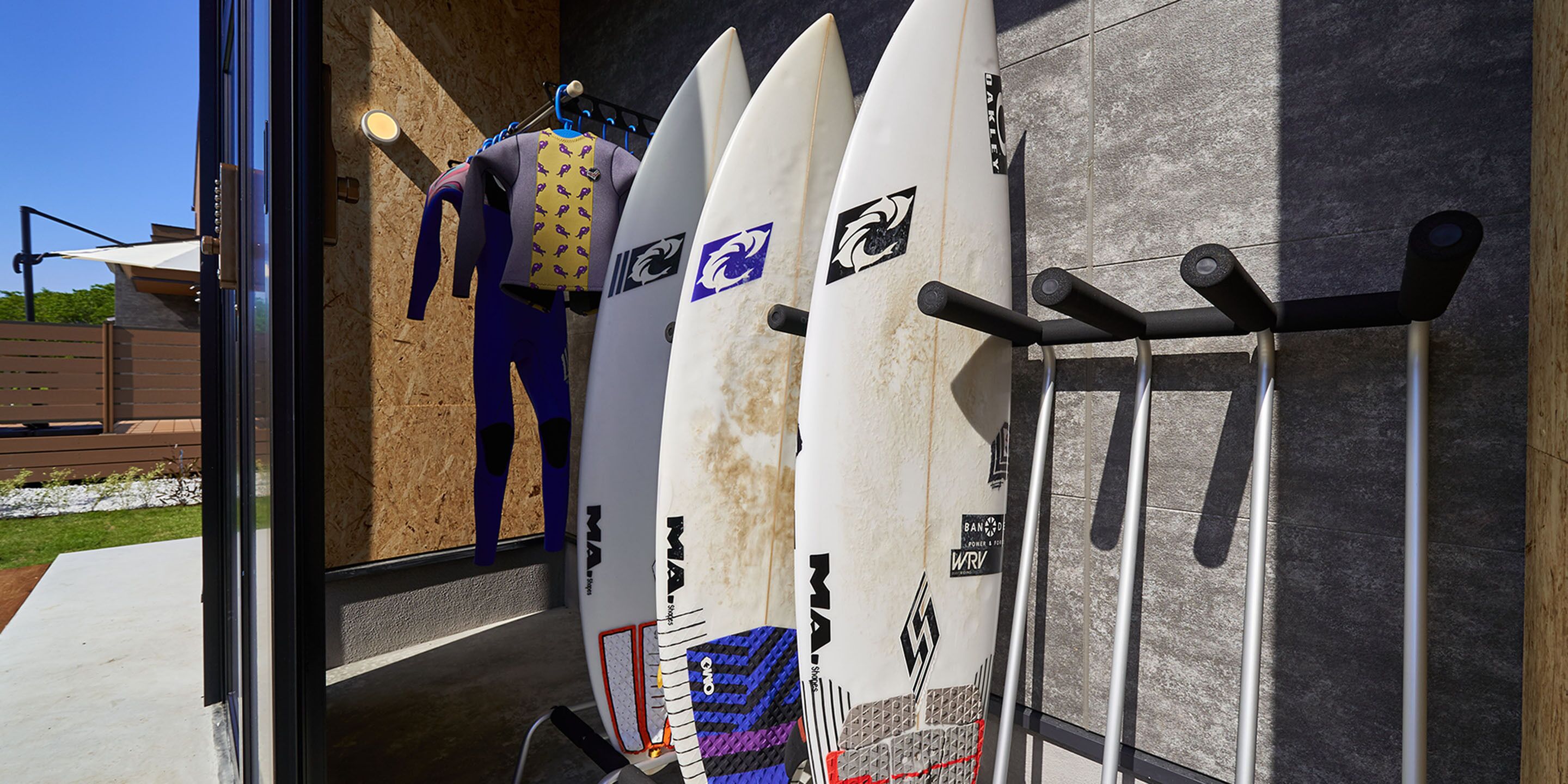 A glass door leading to a room with surfboards and wetsuits hanging on a rack.