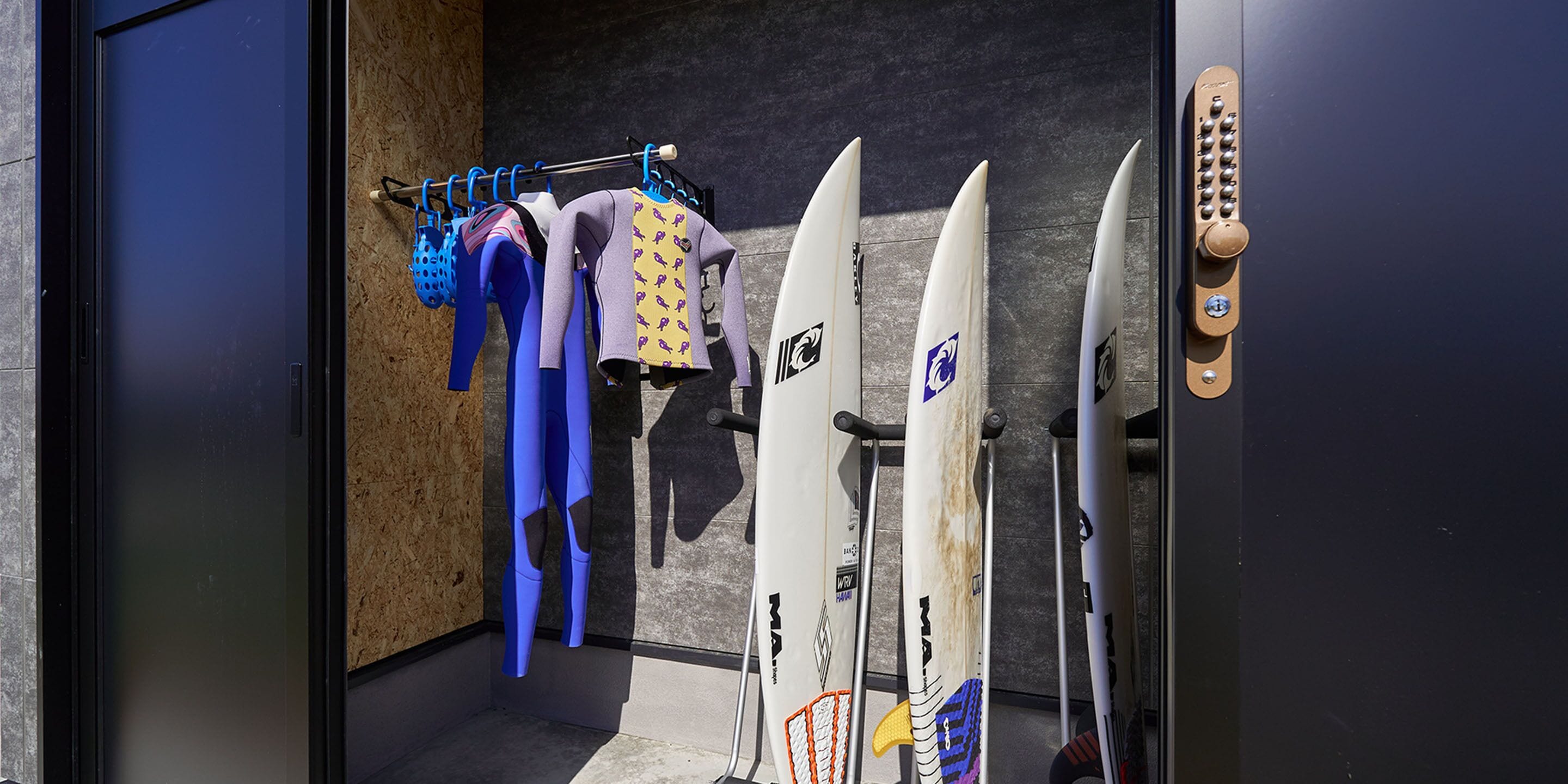 A room with surfboards and wetsuits hanging on a rack.