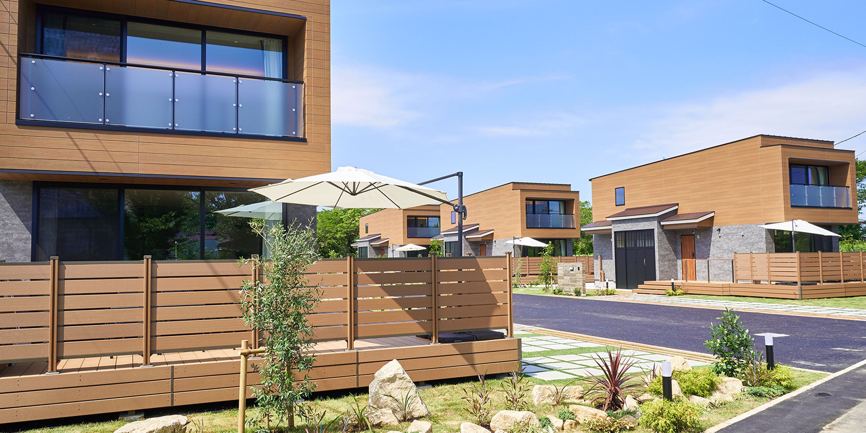 A modern residential building with a wooden facade, a balcony, and a paved driveway.