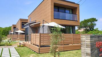 A modern two-story house with a wooden facade, large windows, and a visible balcony.