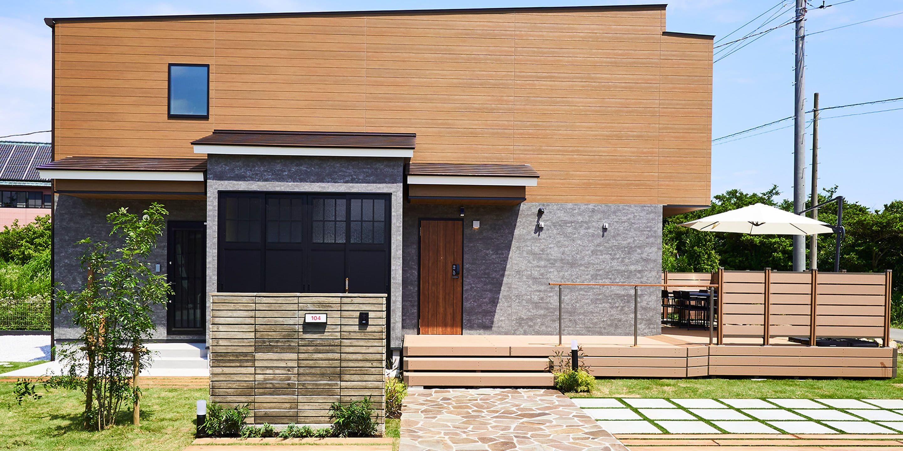 A modern two-story house with a wooden facade, a garage door, and a small patio area with a table and chairs.