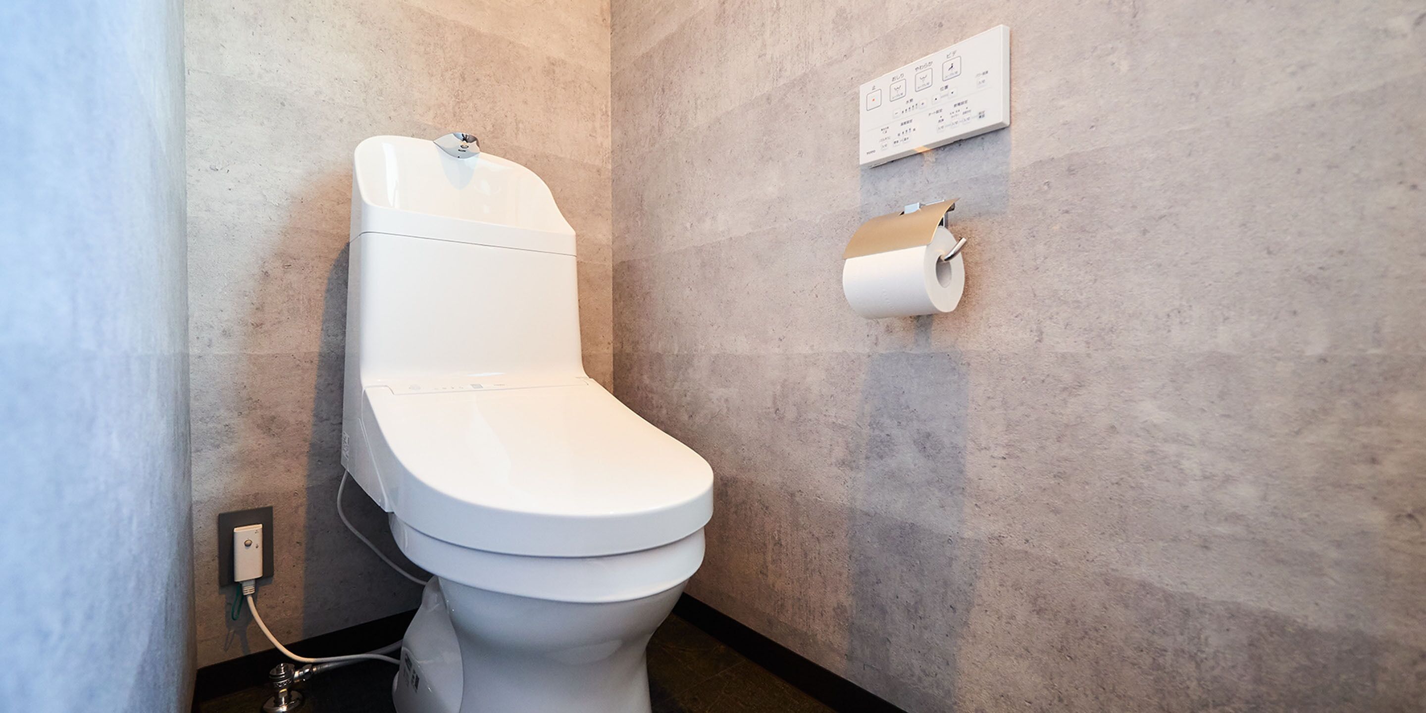 A modern toilet with a control panel, a toilet paper holder, and a wall-mounted sign.