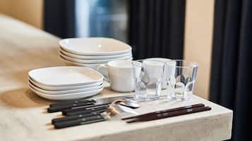A table with stacked white plates, clear glasses, black-handled knives, and a pair of chopsticks.