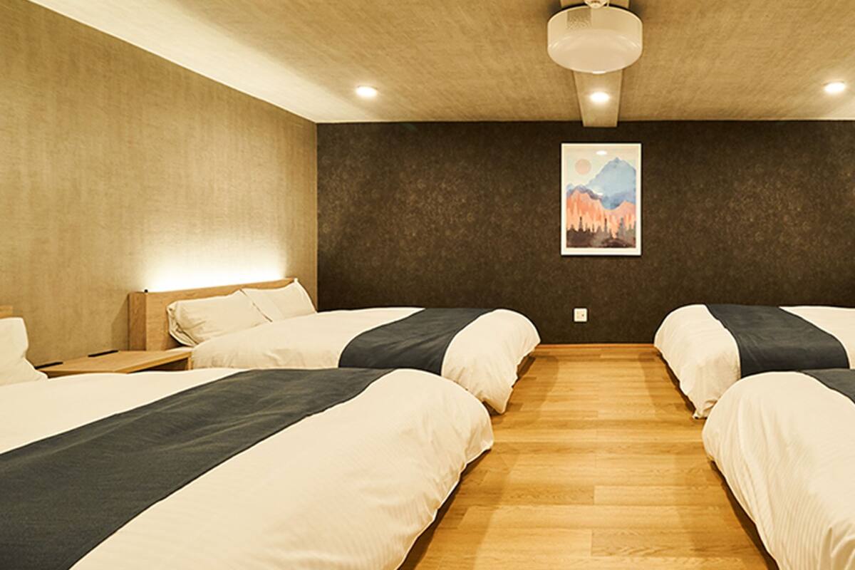 A hotel room with two beds, wooden flooring, a painting on the wall, and an air conditioning unit.