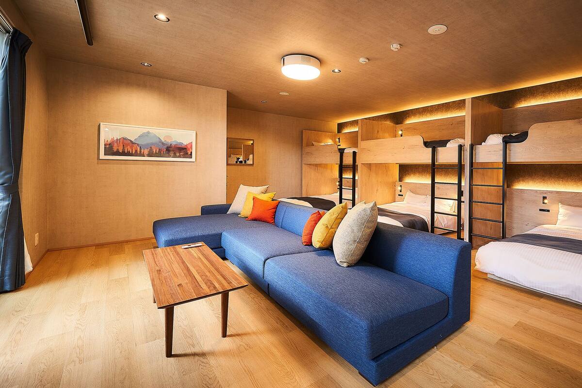 A modern hotel room with a blue sofa, bunk beds, wooden flooring, and a painting on the wall.