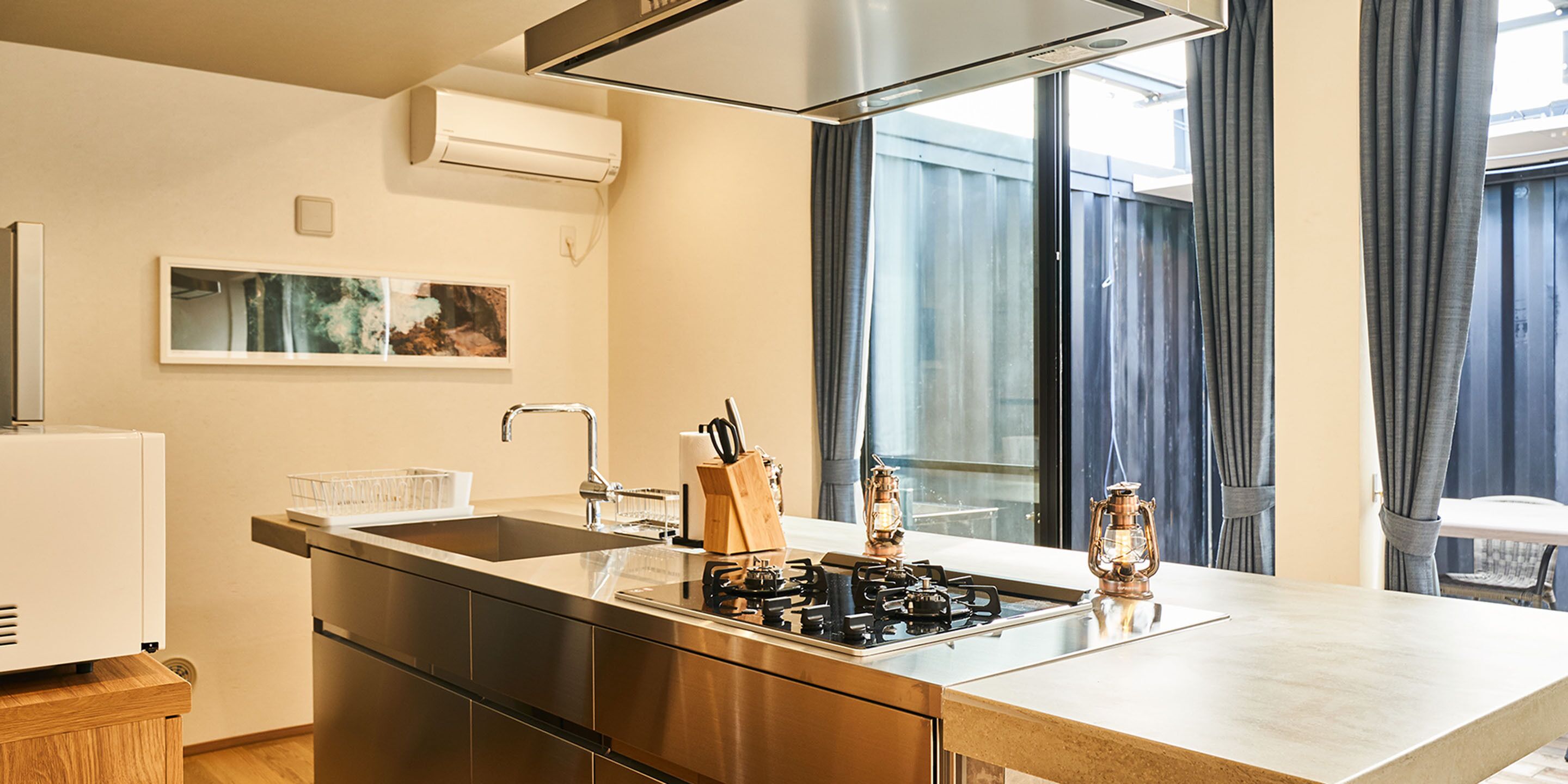 A modern kitchen with a stainless steel range, a built-in sink, and a large window with curtains.