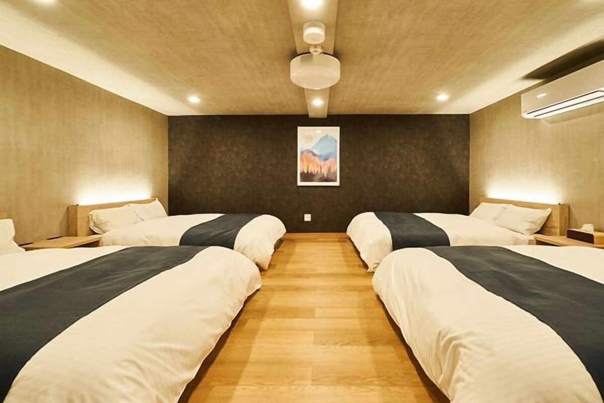 A hotel room with two beds, a wooden floor, a ceiling fan, and a wall-mounted air conditioner.