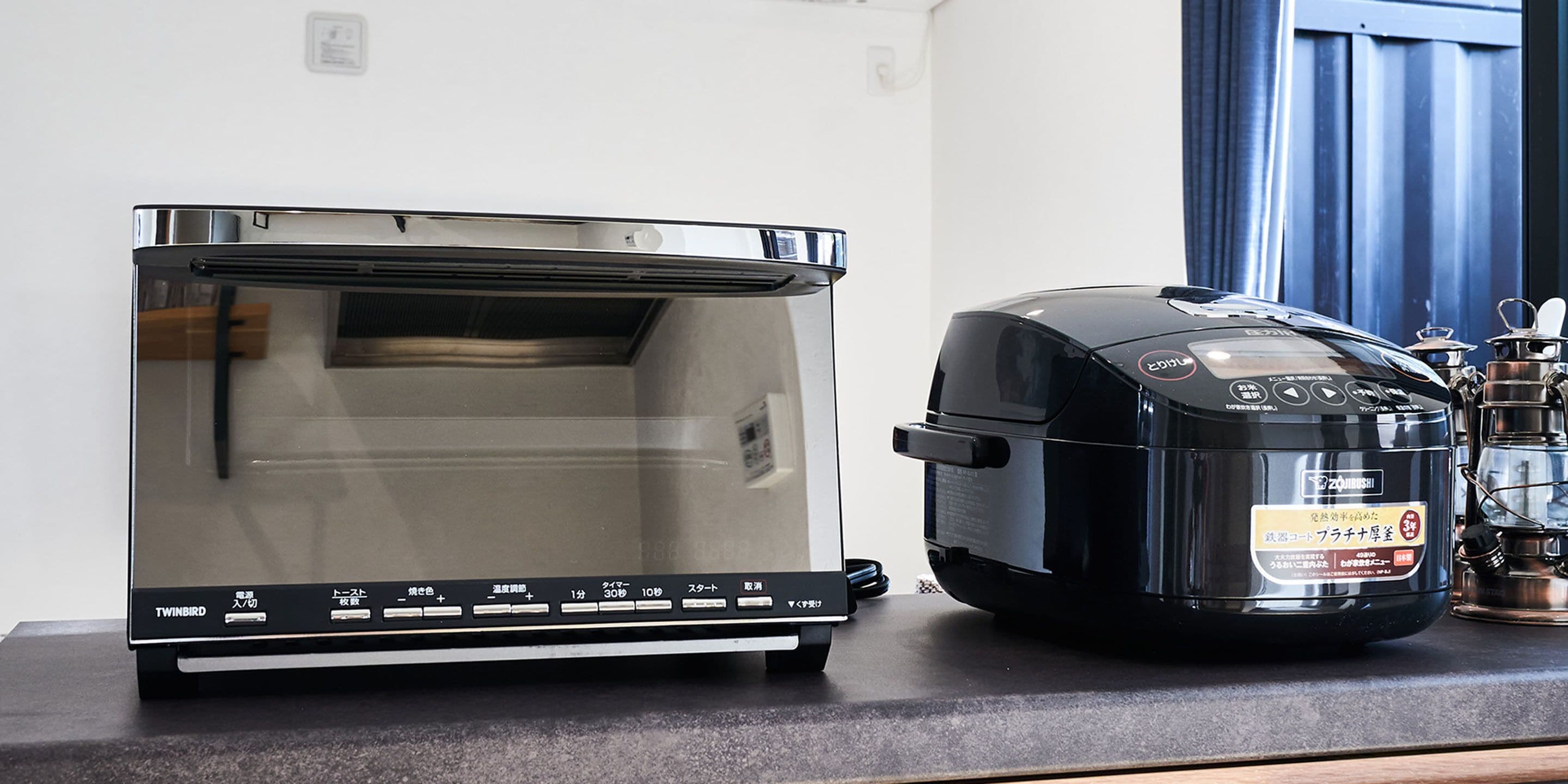 A kitchen with a stainless steel toaster oven and a black rice cooker on the counter.