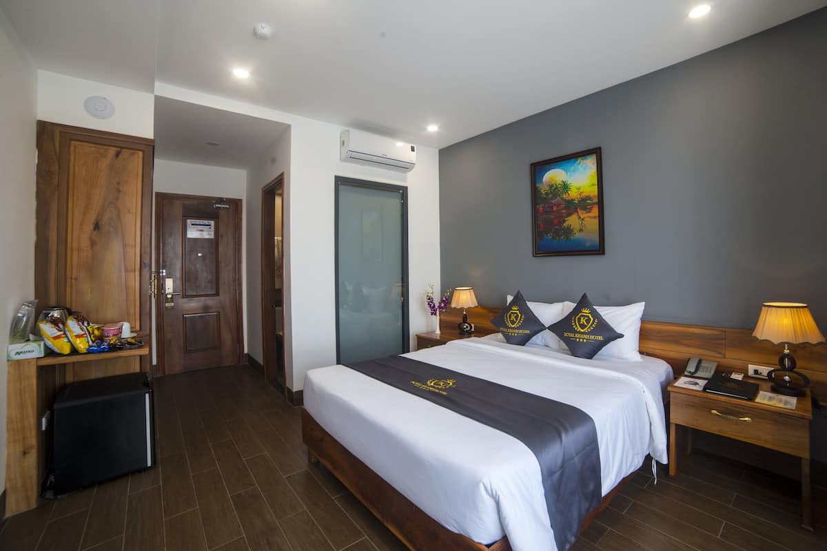 Une chambre d’hôtel avec un grand lit, une armoire en bois, un bureau avec une lampe et un tableau au mur.