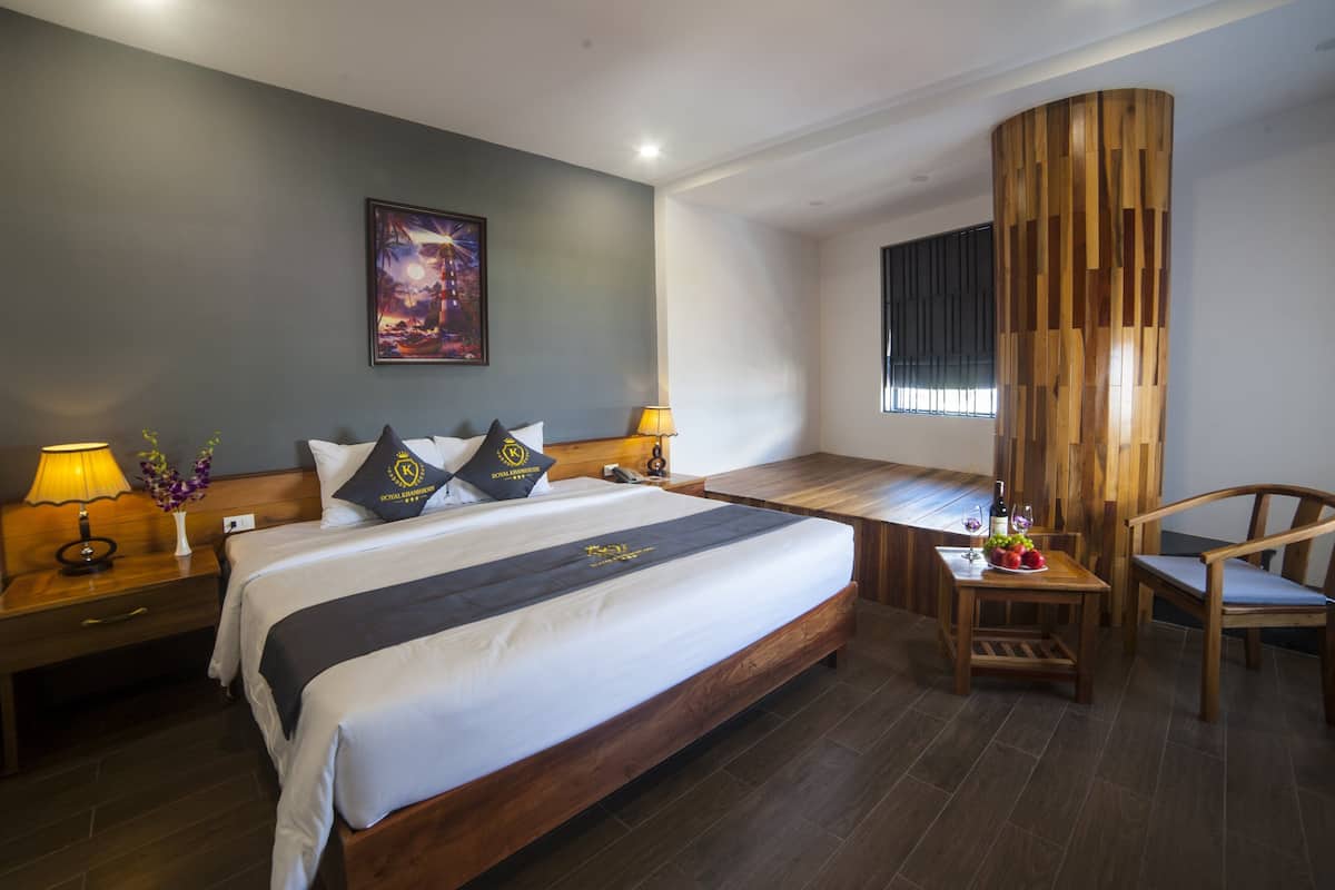 Une chambre d’hôtel avec un grand lit, une tête de lit en bois, un bureau avec une chaise, une lampe et un tableau au mur.