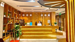 Zona de recepción de un hotel con un mostrador de madera, una recepcionista y una pared que exhibe relojes y nombres de ciudades.