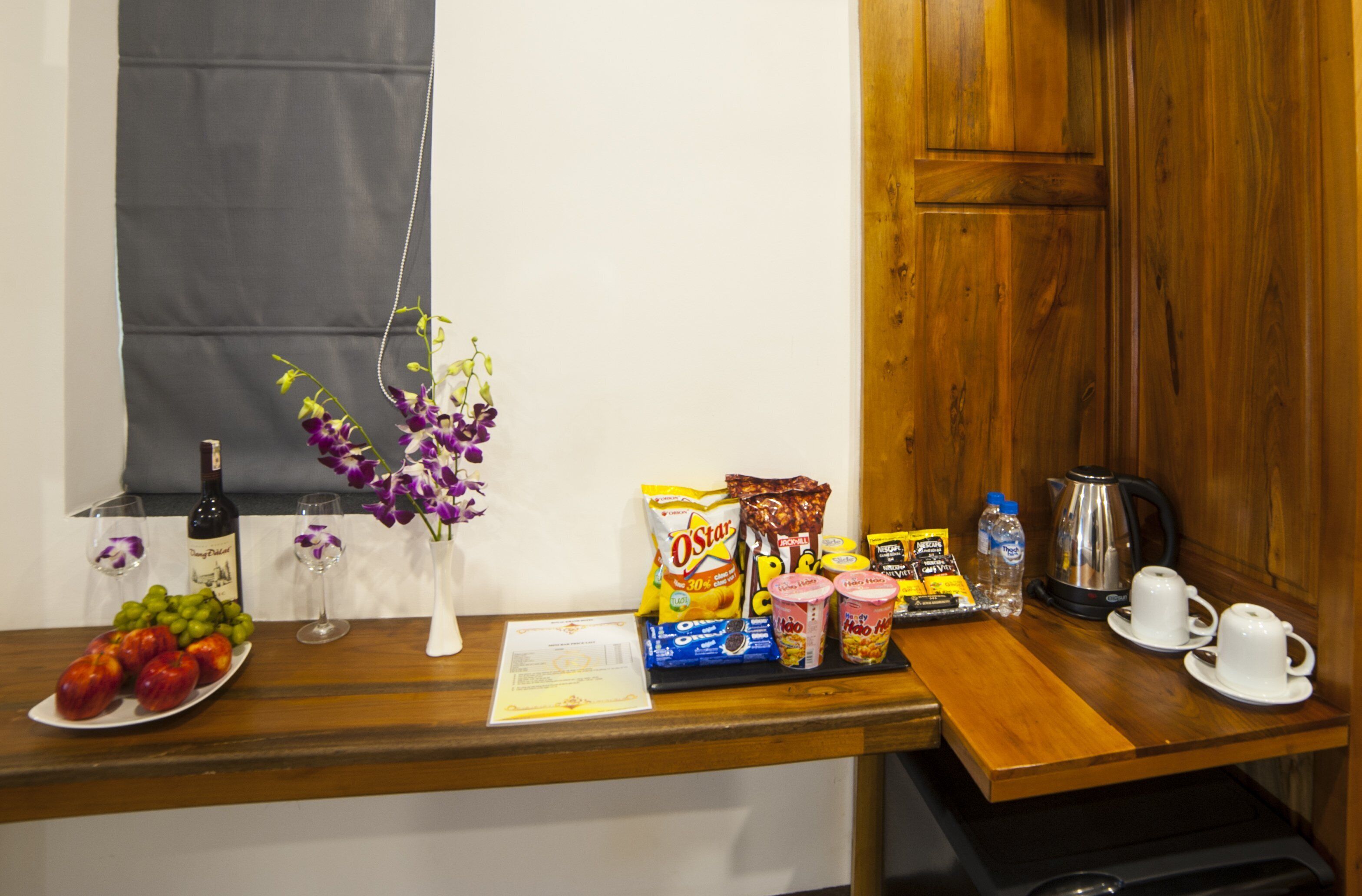 A hotel room's breakfast bar with fruits, a bottle of wine, coffee, tea, and snacks.
