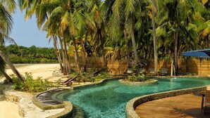 A pool area with a stone border, surrounded by palm trees and a wooden deck.