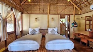 A room with two beds, wooden flooring, a thatched roof, and a wooden bench.