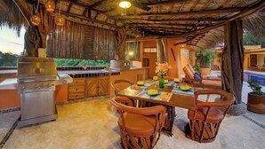 An outdoor dining area with a grill, wicker chairs, and a thatched roof. - Rarely Available- Casa Quixote - Beachfront Estate (Zihuatanjeo)