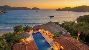 A resort with a swimming pool, thatched-roof structures, and a view of the sea. - Rarely Available- Casa Quixote - Beachfront Estate (Zihuatanjeo)