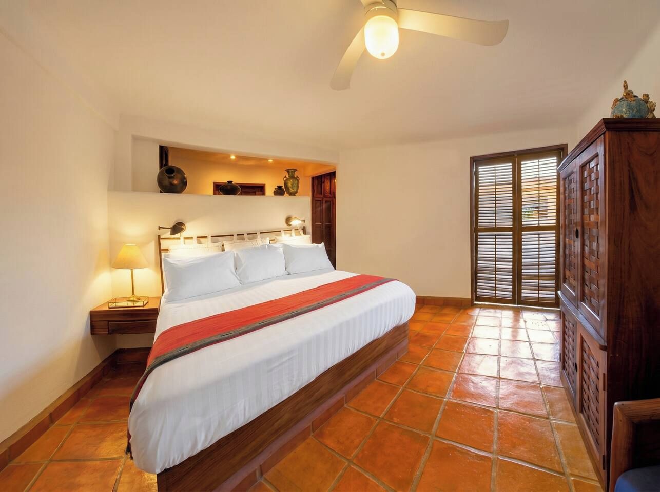 A bedroom with a large bed, a nightstand, a lamp, a ceiling fan, and a view through a door.