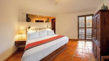A bedroom with a large bed, a nightstand, a lamp, a ceiling fan, and a view through a door.