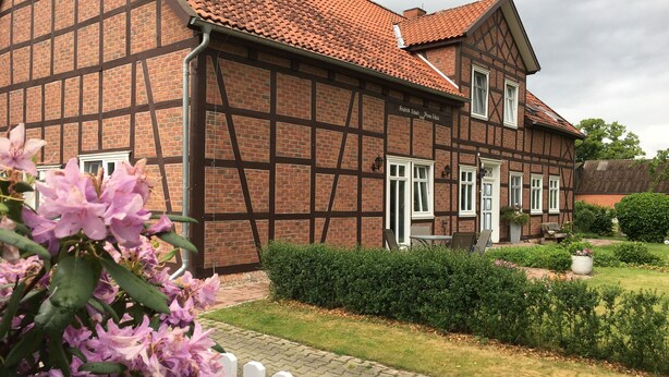 Una casa tradicional con entramado de madera y fachada de ladrillo, ventanas con marcos blancos y un jardín bien cuidado.