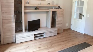 Una sala moderna con un televisor sobre un mueble de madera, un aparador de vidrio y una puerta con panel de vidrio satinado.