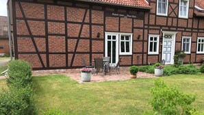 Un edificio tradicional de entramado de madera con fachada de ladrillo, un patio empedrado con mesas al aire libre y un jardín cuidado.