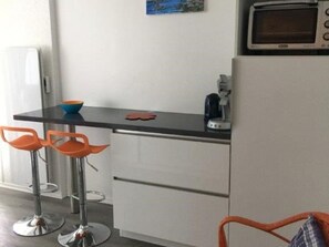 A compact kitchen with a microwave, a coffee maker, and two orange bar stools.