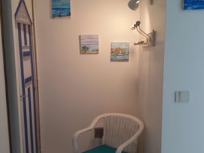 A room with a white wicker chair, a door with a blue and white striped pattern, and three small paintings on the wall.