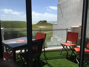 A balcony with a table and chairs, a view of a hill and a castle, and a white wall.