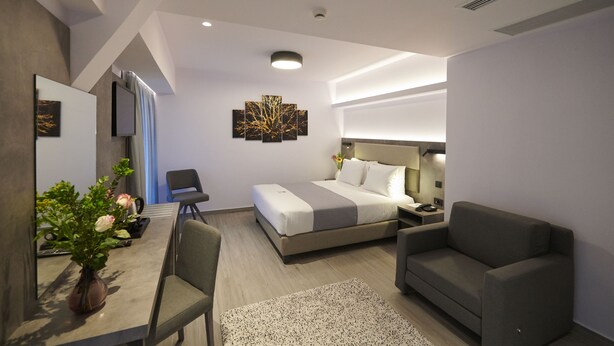 Quarto de hotel moderno com cama, escrivaninha, cadeira, sofá e televisão de tela plana.