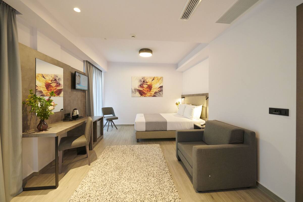 Ein modernes Hotelzimmer mit einem Bett, einem Schreibtisch, einem Sessel, einer Couch und Bildern an der Wand.