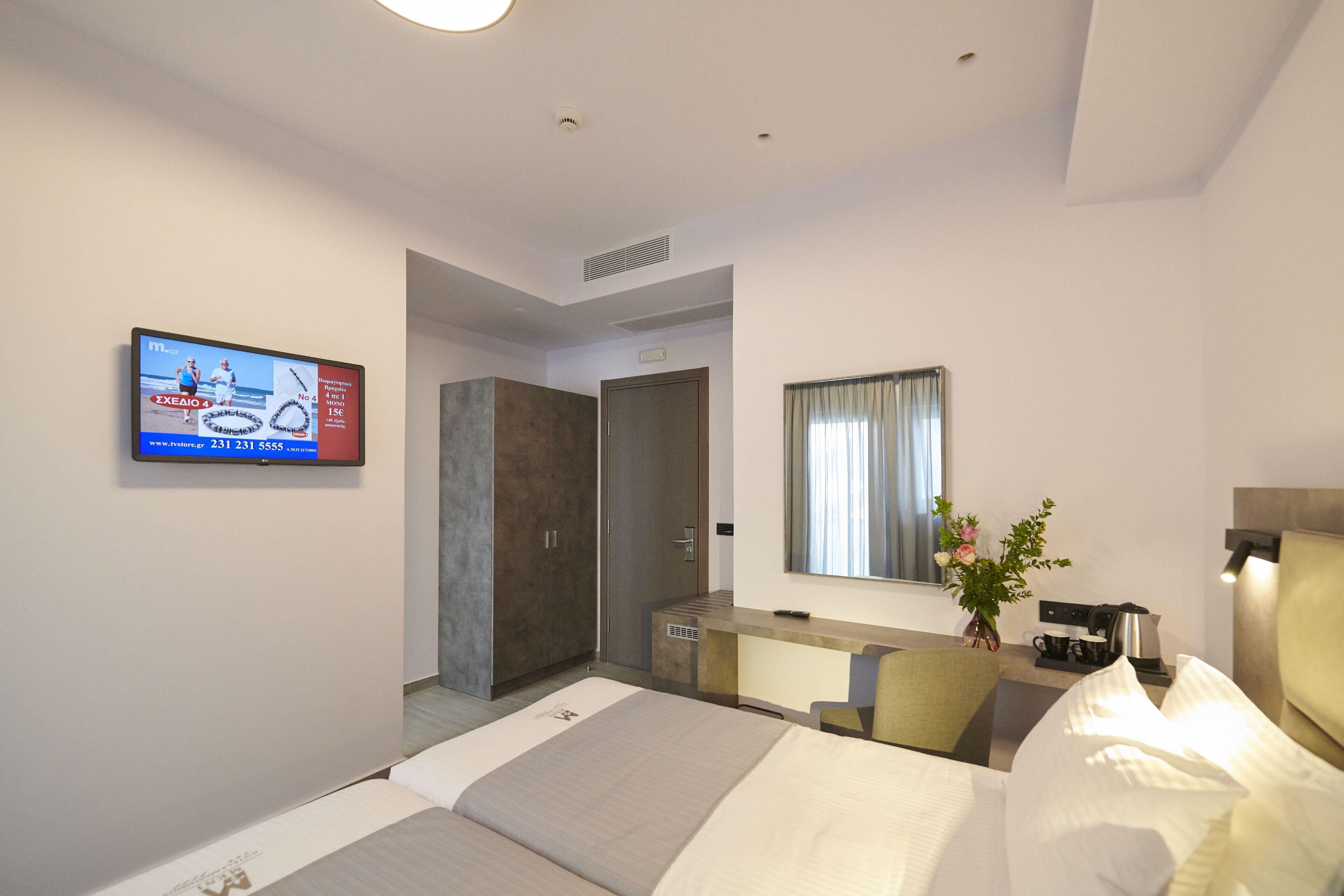 A hotel room with a bed, a desk with a chair, a mirror, a television, and a small plant.