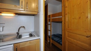 A compact kitchen with wooden cabinets, a stainless steel sink, and a built-in dishwasher. - Cozy studio with balcony, ski-in/ski-out (Les Menuires)