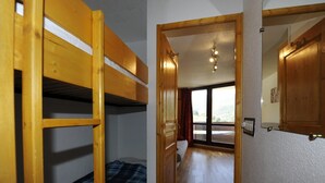 A room with bunk beds, a wooden door, and a view of a balcony. - Cozy studio with balcony, ski-in/ski-out (Les Menuires)