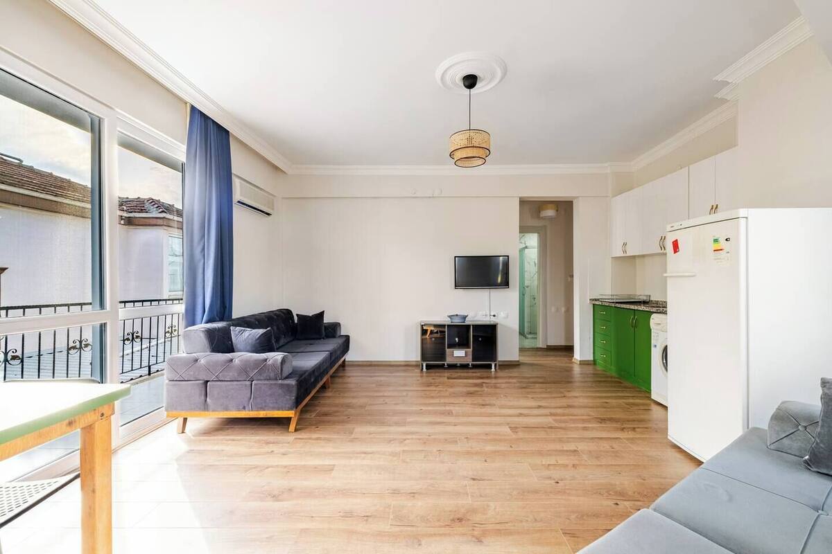 Un apartamento moderno con un sofá gris, un televisor pequeño y una cocina con armarios verdes.