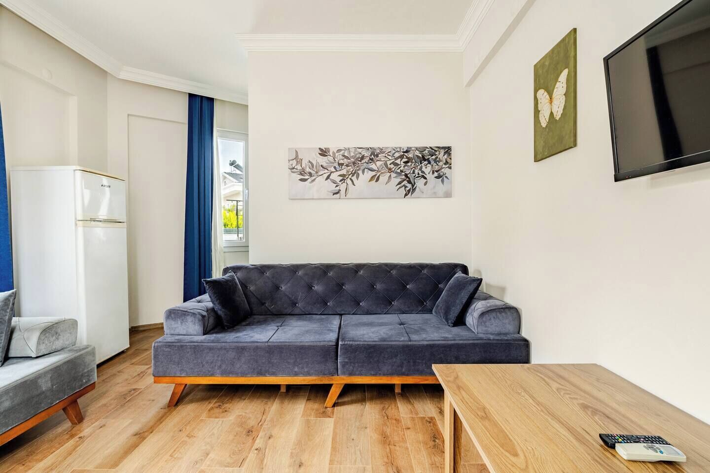 A modern living room with a grey sofa, a wooden coffee table, and a flat-screen TV mounted on the wall.