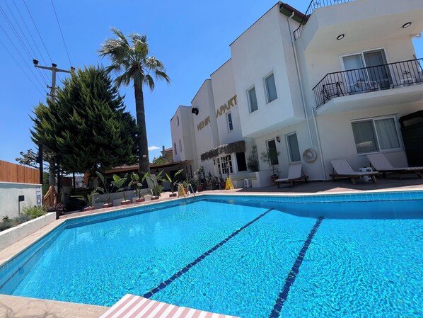 A swimming pool with clear blue water, surrounded by potted plants and a building with a balcony.